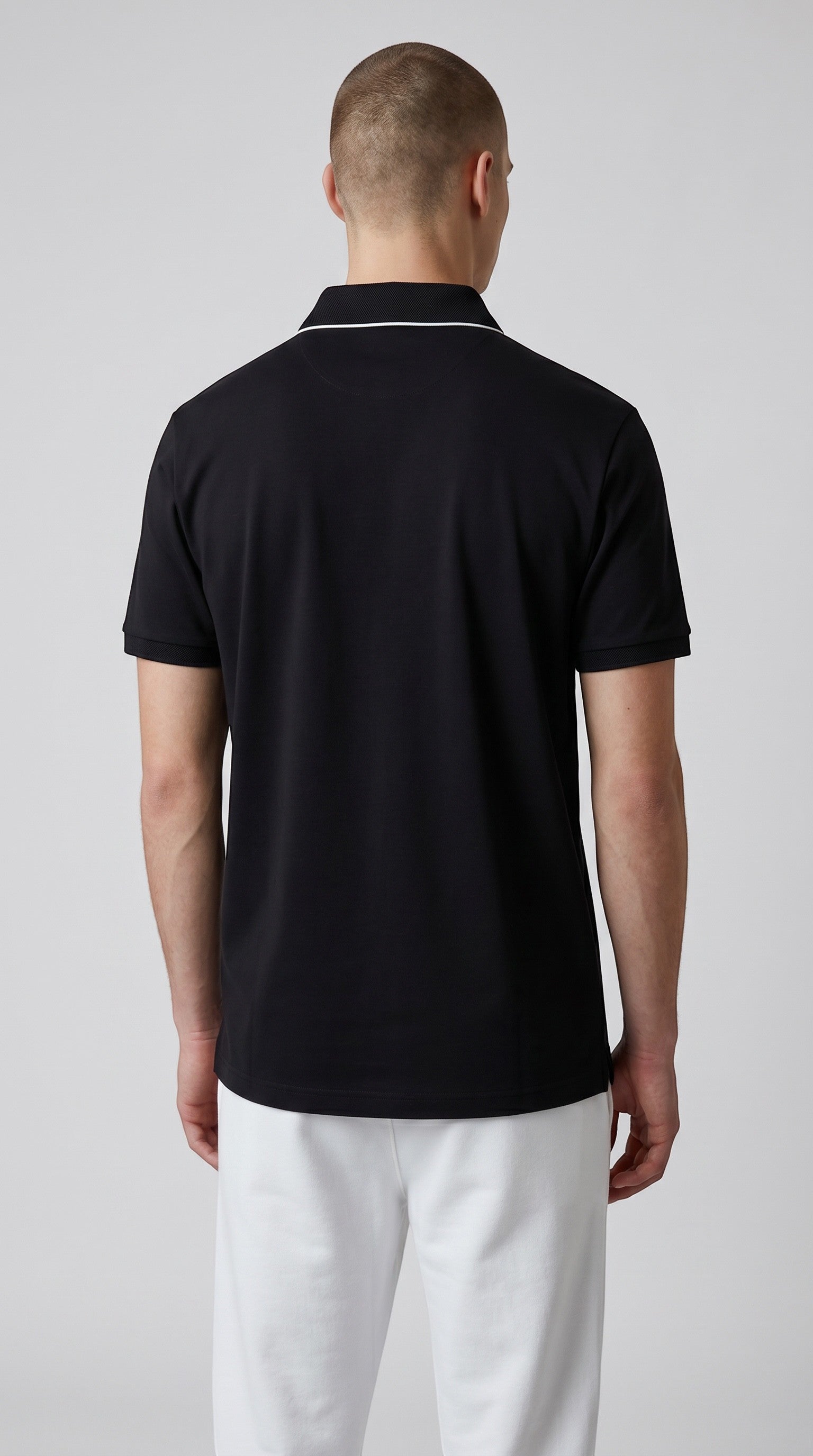 Back view of a man wearing a black Eclipse-The Label polo shirt with white collar trim and white shorts