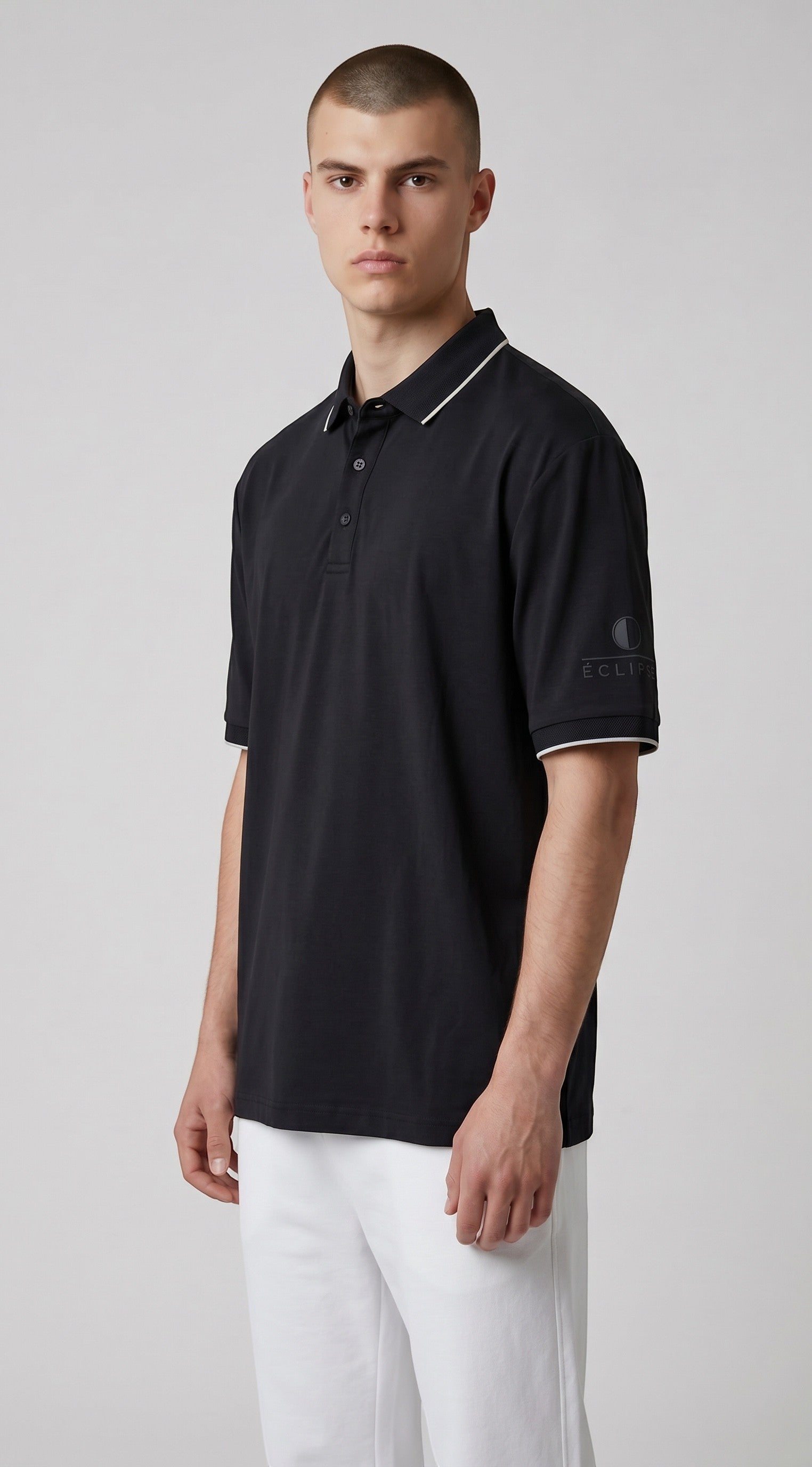 Male model wearing an Eclipse-The Label black polo shirt with white collar and sleeve trim and logo on the left sleeve.